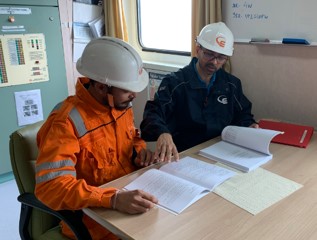 Two seafarers sitting at a table going over manuals and documents.